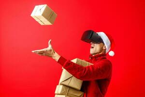 homme portant et en jouant mobile Jeu app sur dispositif virtuel réalité des lunettes sur rouge Contexte. portrait de un Beau Nouveau année homme dans rouge Père Noël claus Noël chapeau avec fourrure photo
