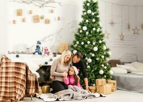 Nouveau an. Noël. famille. Jeune Parents et leur peu fille dans Père Noël Chapeaux sont dépenses temps ensemble près le Noël arbre à Accueil photo