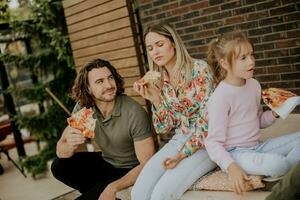 Jeune famille en mangeant Pizza dans le maison arrière-cour photo