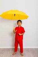 peu garçon mode une souriant enfant en portant une Jaune parapluie dans une rouge chinois robe. chinois Nouveau année, chinois Nouveau année photo