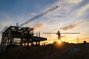 une construction ouvrier dans construction site à le coucher du soleil dans soir temps. silhouette de construction. photo