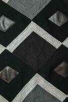 détaillé inserts dans noir authentique cuir sur une tricoté de laine Contexte avec un abstrait modèle. abstrait en tissu texture. photo