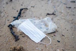 masque usagé pendant covid 19 a été jeté sur la plage de sable. le sujet est ébavuré. photo