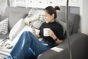 belle jeune femme se reposant sur un canapé à la maison et utilisant un téléphone intelligent photo