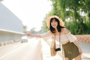 portrait de asiatique Jeune femme voyageur avec tissage chapeau et panier et une caméra agitant main à ami par le rue. périple voyage mode de vie, monde Voyage explorateur ou Asie été tourisme concept. photo