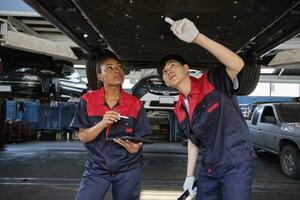 deux professionnel automobile ouvrier les partenaires discuter mécanique vérifier châssis de levé électrique voiture, réparer et réparation à entretien garage, et expert un service affaires travaux industrie profession. photo