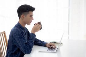 jeune homme d'affaires travaillant à domicile avec un ordinateur portable sur le bureau, un homme indépendant assis reste à la maison en utilisant un ordinateur portable pour communiquer et se détendre sur la table, entrepreneur en démarrage d'entreprise, nouvelle normalité. photo