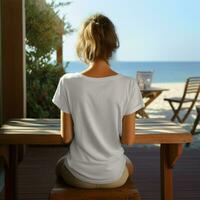 ai généré femme asseoir sur le plage café, portant une Vide blanc T-shirt, orienté vers en arrière photo