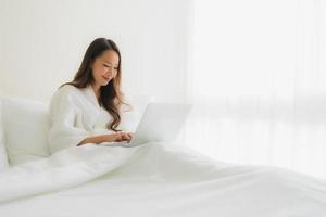 Portrait de belles jeunes femmes asiatiques avec une tasse de café et un ordinateur portable sur le lit photo