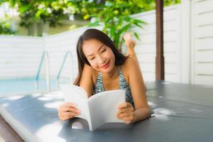 Portrait belle jeune femme asiatique sourire heureux avec livre de lecture autour de la piscine photo