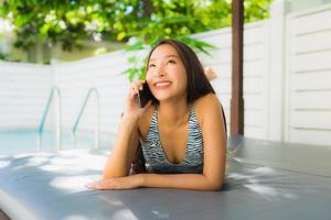 Portrait belle jeune femme asiatique sourire heureux parler téléphone portable autour de la piscine photo