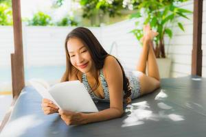 Portrait belle jeune femme asiatique sourire heureux avec livre de lecture autour de la piscine photo