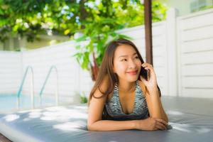 Portrait belle jeune femme asiatique sourire heureux parler téléphone portable autour de la piscine photo