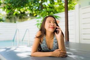 Portrait belle jeune femme asiatique sourire heureux parler téléphone portable autour de la piscine photo