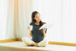 Portrait belle jeune femme asiatique lisant un livre et tenant une tasse de café ou une tasse sur le canapé dans le salon photo