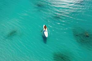 aérien vue de une femme dans une blanc chapeau avec une planche de surf dans le océan, aérien vue de une femme sur une planche de surf dans le turquoise des eaux de le Maldives, ai généré photo