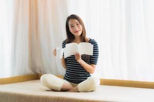 Portrait belle jeune femme asiatique lisant un livre et tenant une tasse de café ou une tasse sur le canapé dans le salon photo