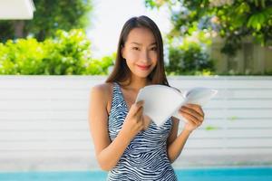 Portrait belle jeune femme asiatique sourire heureux avec livre de lecture autour de la piscine photo