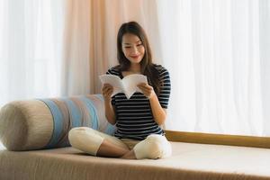 Portrait belle jeune femme asiatique lisant un livre sur un canapé dans le salon photo