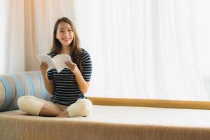 Portrait belle jeune femme asiatique lisant un livre sur un canapé dans le salon photo