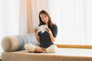 Portrait belle jeune femme asiatique lisant un livre sur un canapé dans le salon photo