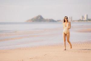 Portrait jeune belle femme asiatique à pied sourire heureux sur la plage mer océan avec des lunettes de soleil photo