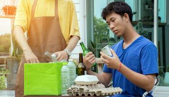 Jeune Beau asiatique gay des couples sont séparer ménages, bouteilles, canettes, poubelle, papier, Oeuf plateau, dans de face de leur loger, environnement se soucier et global chauffage concept. photo