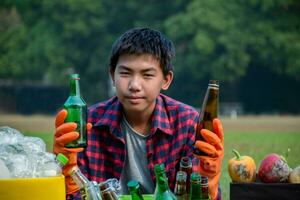 asiatique garçon dans plaid chemise séance sur terrain de jeux de école avec divers des boites de séparé les ordures ou poubelles à l'intérieur, concept pour éco copains et global chauffage campagne, doux et sélectif se concentrer. photo