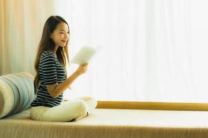 Portrait belle jeune femme asiatique lisant un livre sur un canapé dans le salon photo