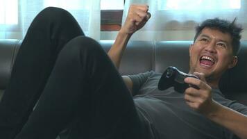 asiatique Jeune homme ayant amusement en jouant vidéo Jeux asseoir canapé à maison. photo
