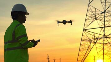 silhouette de électrique ingénieur forcer une drone à inspecter haute Tension poteaux pendant le le coucher du soleil temps. photo