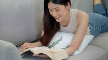magnifique asiatique Jeune femme en train de lire livre sur canapé à maison. photo