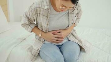 asiatique Jeune femme Souffrance de abdominal douleur tandis que séance dans lit à maison. photo