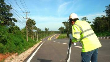 arpenteur ingénieur avec théodolite sur route Autoroute pendant le ensoleillé journée avec route dans Contexte. photo