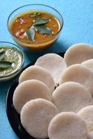 idli avec sambar et chutney de noix de coco sur fond bleu, plat indien plat préféré de l'Inde du Sud rava idli ou semoule oisivement ou rava oisivement, servi avec sambar et chutney de noix de coco verte. photo