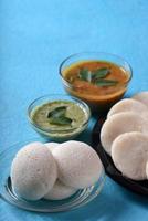 idli avec sambar et chutney de noix de coco sur fond bleu, plat indien plat préféré de l'Inde du Sud rava idli ou semoule oisivement ou rava oisivement, servi avec sambar et chutney de noix de coco verte. photo