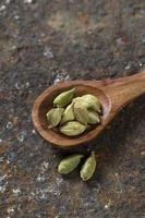 gousses de cardamome dans une cuillère en bois sur un fond texturé photo