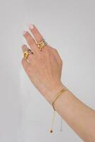 femme main portant serpent chaîne bracelets et interverrouillé d'or et argent anneaux ensemble contre une blanc Contexte. magnifique la Saint-Valentin cadeau. photo