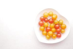 Tomate cerise couleur sur plaque en forme de coeur sur fond blanc photo