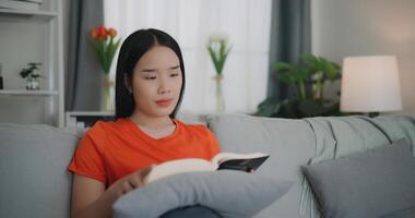 asiatique femme en train de lire une livre tandis que séance sur le canapé photo