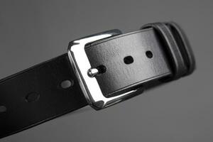partie de une noir cuir ceinture avec une métal Boucle fermer sur une gris Contexte. photo