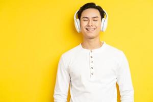 photo d'un homme asiatique en chemise blanche écoutant de la musique les yeux fermés sur fond jaune