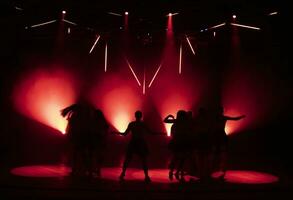 foncé silhouettes de dansant les filles contre le Contexte de rouge lumière de étape projecteurs. photo