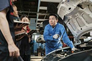 asiatique Masculin professionnel automobile ingénieur superviseur décrit voiture moteur entretien et réparation travail avec mécanicien ouvrier états-majors équipe dans réparer un service garage, spécialiste métiers dans auto industrie. photo