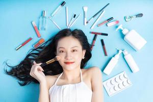 femme asiatique allongée sur fond bleu avec du maquillage autour photo