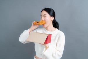 jeune femme asiatique portant un pull avec un visage heureux et aime manger du poulet frit sur fond gris photo