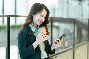 portrait d'une jeune réalisatrice asiatique debout, buvant du café et écoutant le téléphone