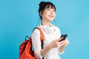 étudiante asiatique portant un sac à dos derrière son dos, tenant un smartphone, le cou portant des écouteurs sans fil, tenant une tasse en papier photo