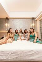 une groupe de asiatique femmes dans magnifique Robes séance ensemble sur une blanc lit tandis que rester photo
