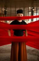 un asiatique homme permanent fièrement parmi le rouge tissu cette se balance dans un vieux bâtiment photo